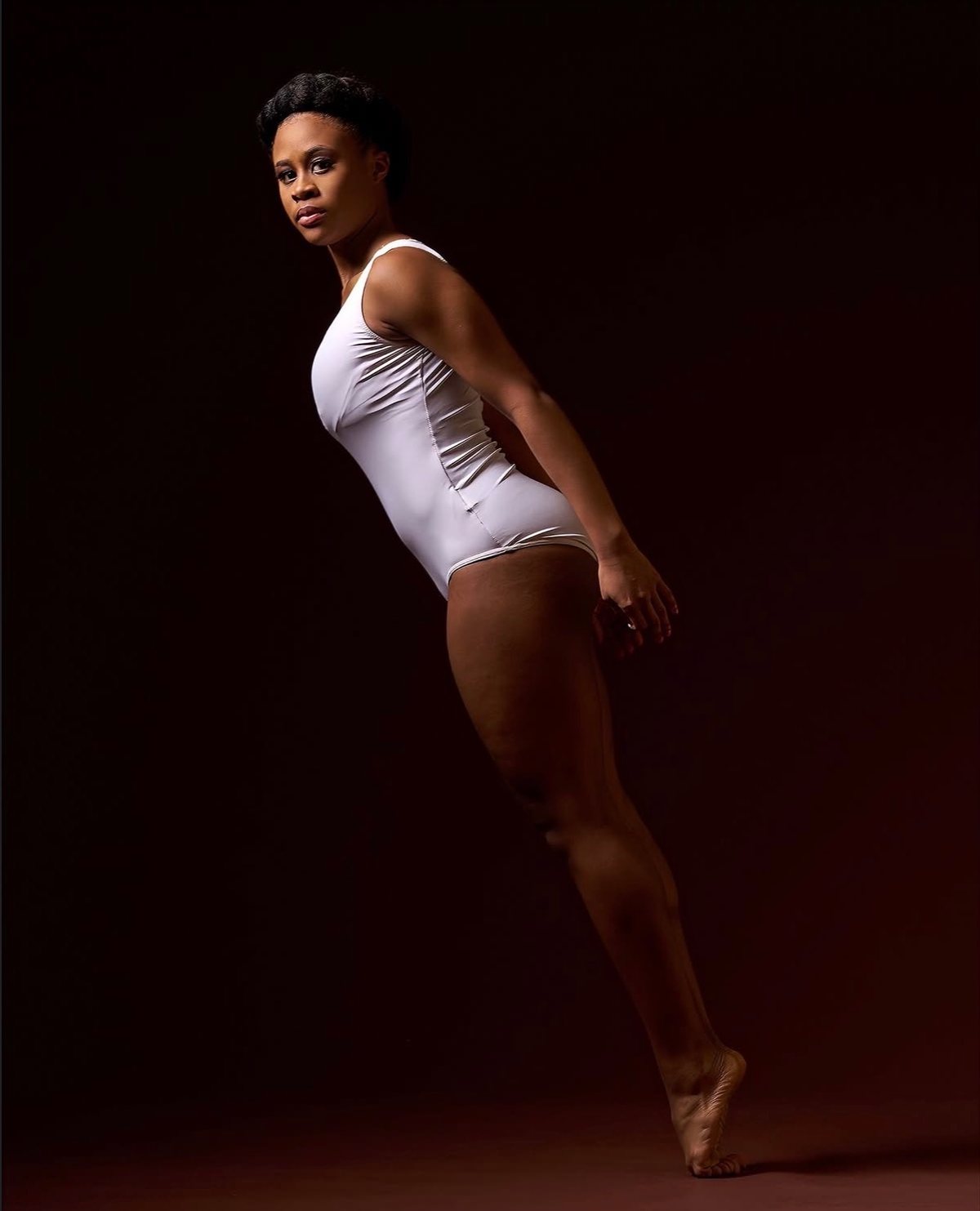 Amoni in white leotard with direct gaze, dramatic dark studio lighting